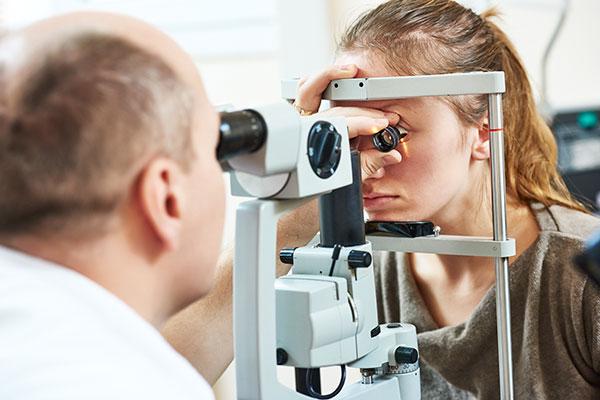 eye doctor performing eye exam on young woman slit lamp fundus lens